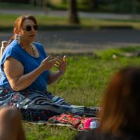 woman seated on the ground on blanket talking to adults, also seated